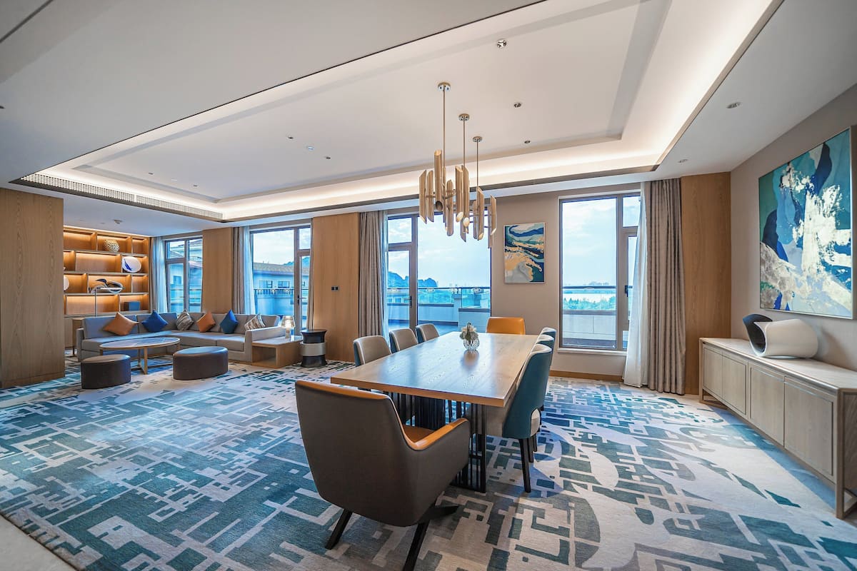 Ein geräumiges Hotelzimmer mit großem Esstisch, bequemen Sitzgelegenheiten, einer modernen Chandelier und großen Fenstern mit Blick auf die Stadt.