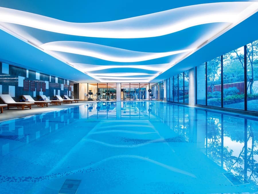 Una piscina interior moderna con vistas despejadas a los alrededores, incluyendo un gimnasio y un área de descanso.