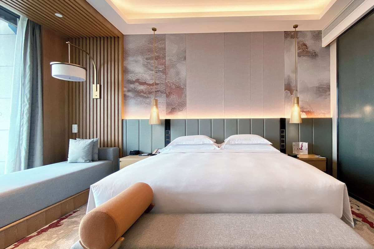 Ein modernes Hotelzimmer mit einem großen Bett, einer Couch, einem Nachttisch und einem an der Wand befestigten Fernseher.