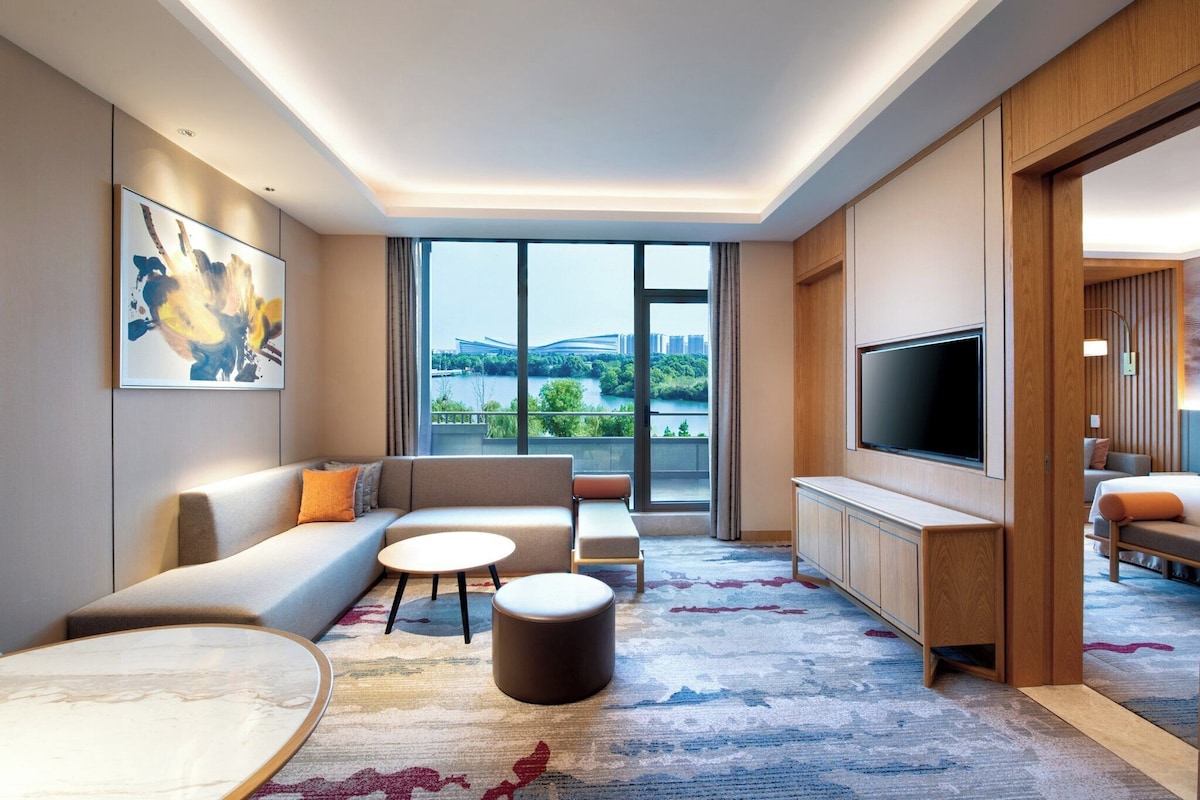 Una habitación de hotel moderna con un ventanal grande, un sofá, un televisor y una mesita de café.