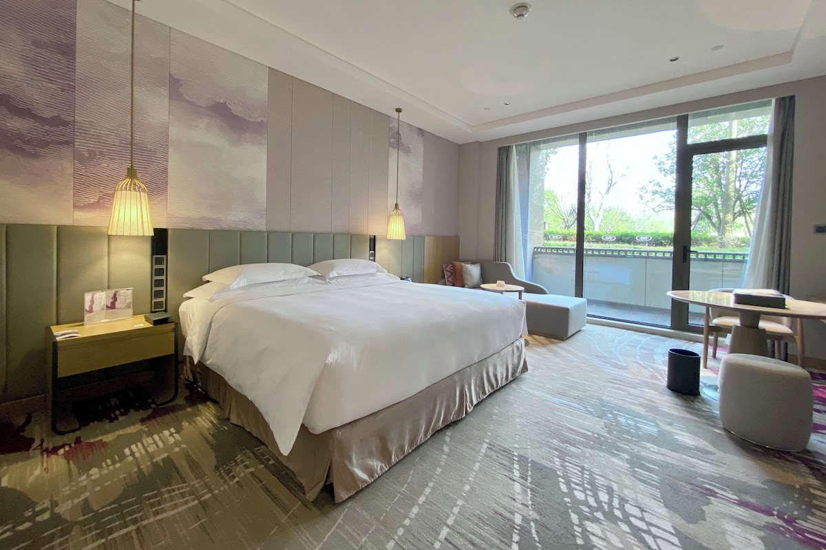 Habitación de hotel moderna con una cama grande, un área de descanso con mesa y un balcón con vistas.
