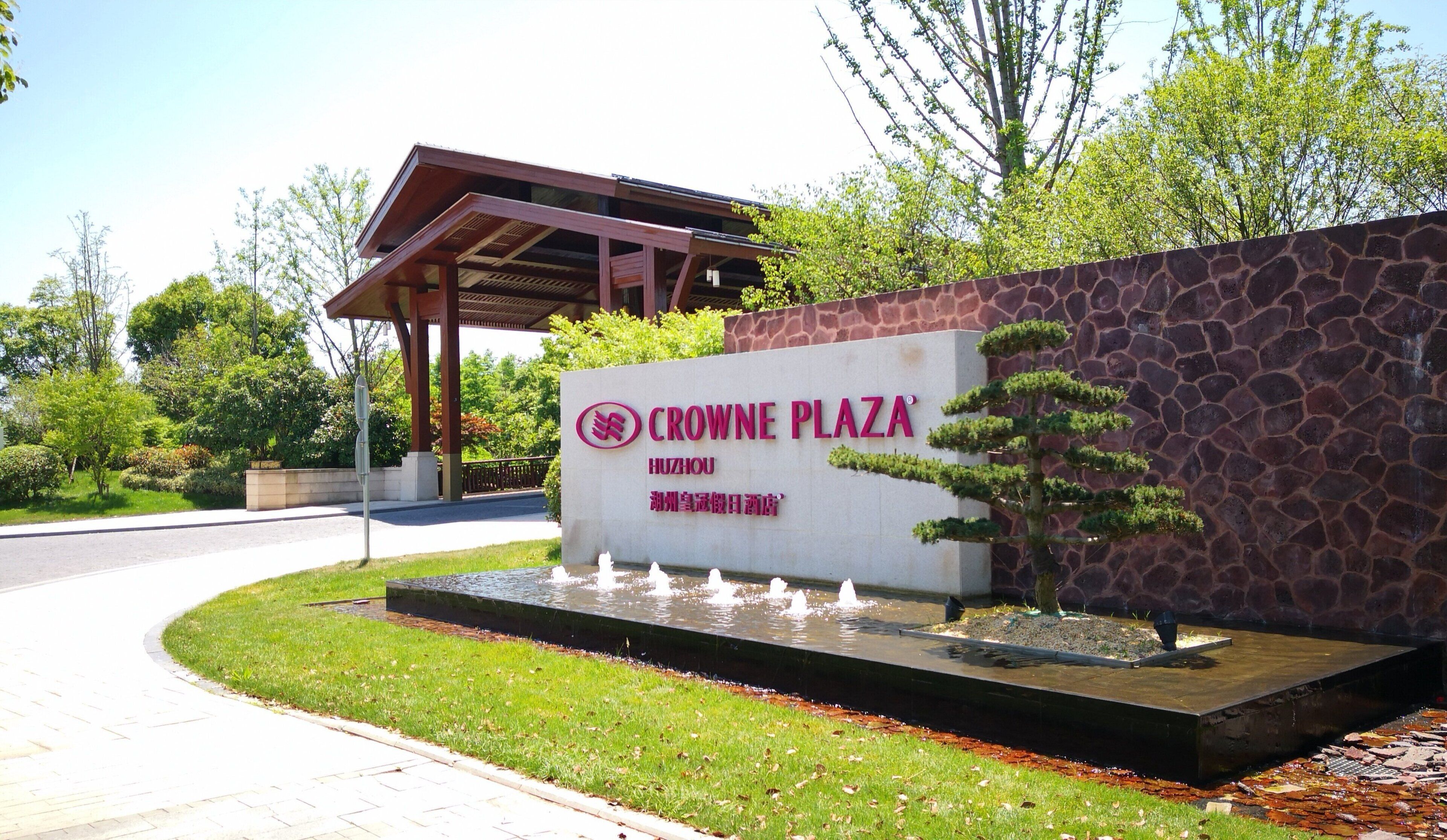Schild für Crowne Plaza Huzhou mit einer Steinmauer und einem Wasserspiel im Vordergrund.
