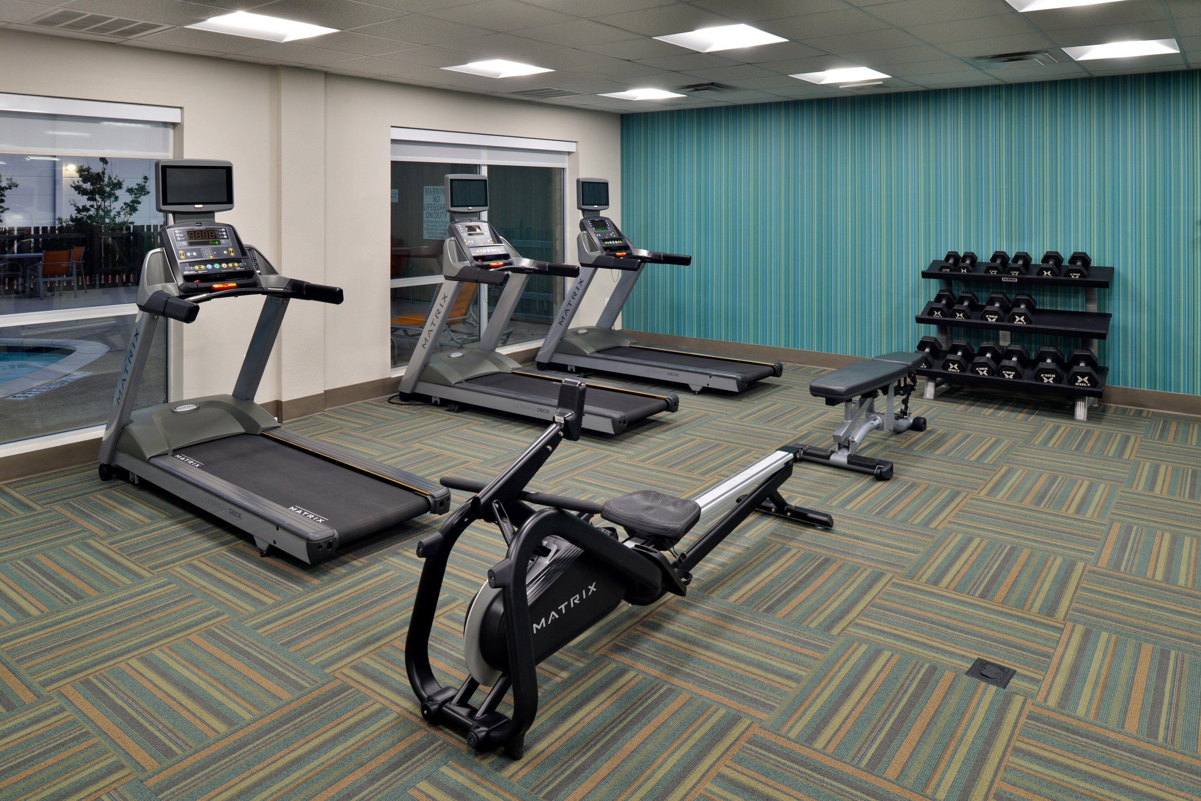 A gym with treadmills, a rowing machine, and dumbbells.