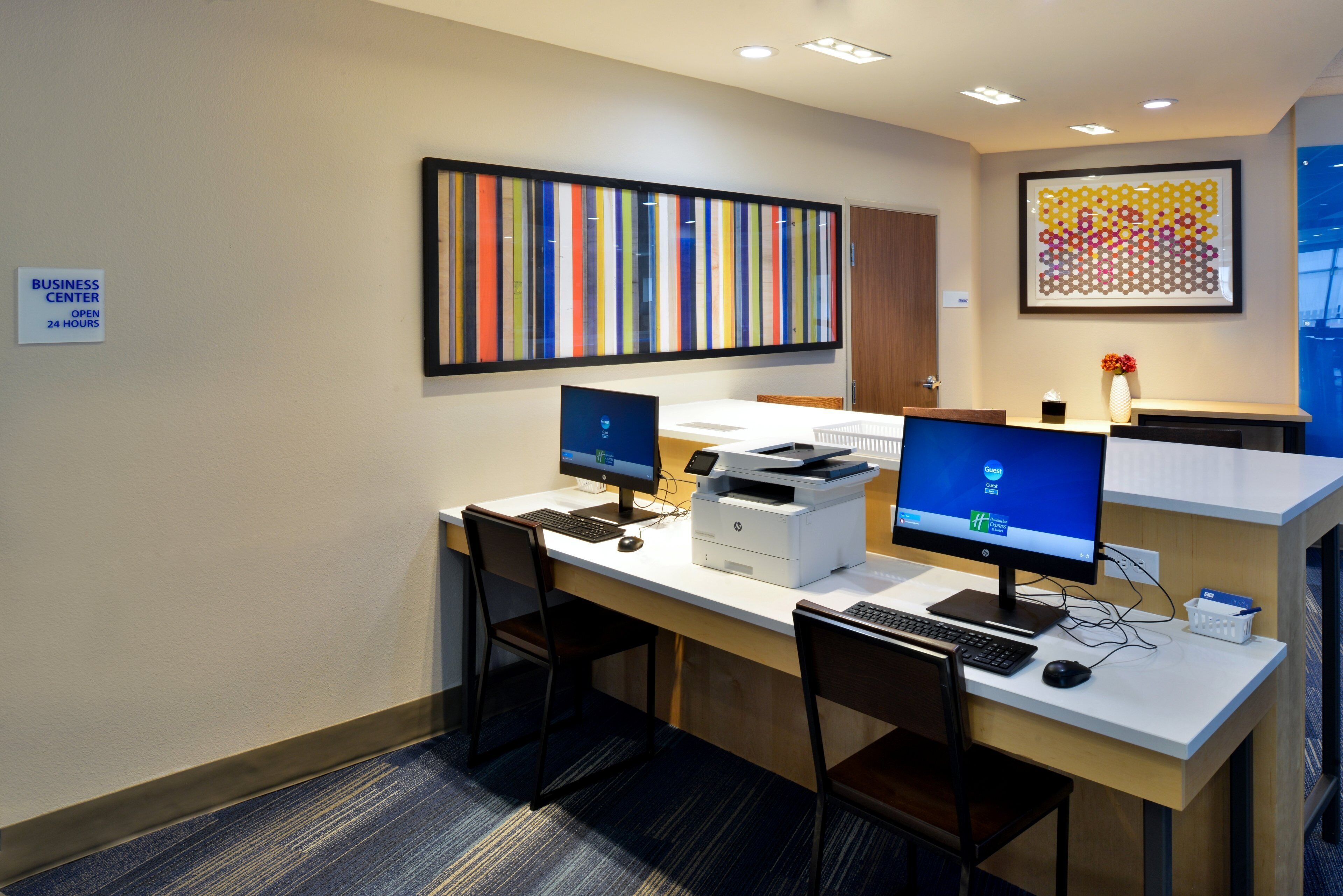 A business center with two computer stations, a printer, and a sign indicating 24-hour availability.