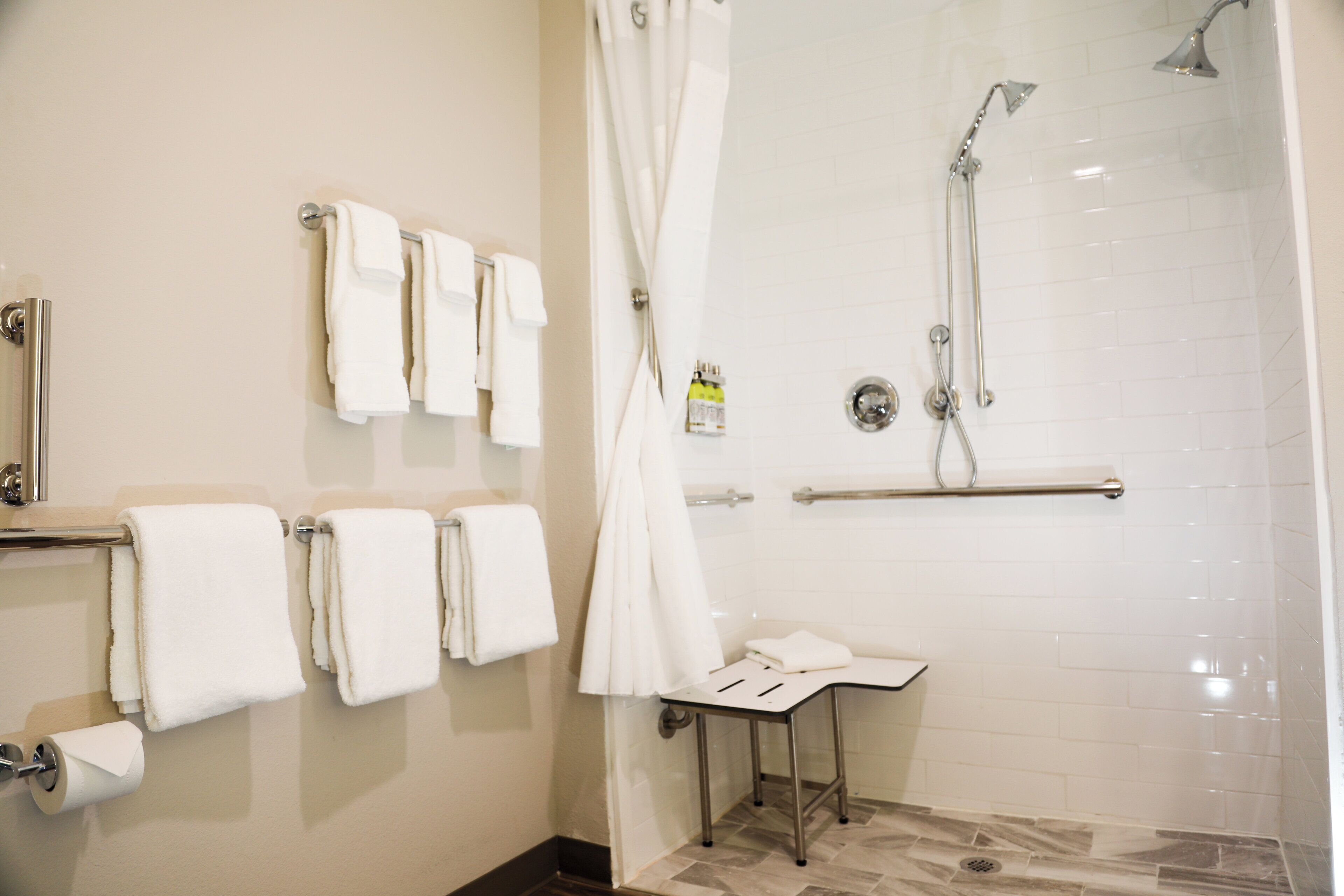Ein Badezimmer mit Dusche, Waschbecken und mehreren Handtüchern an einem Ablagekorb.
