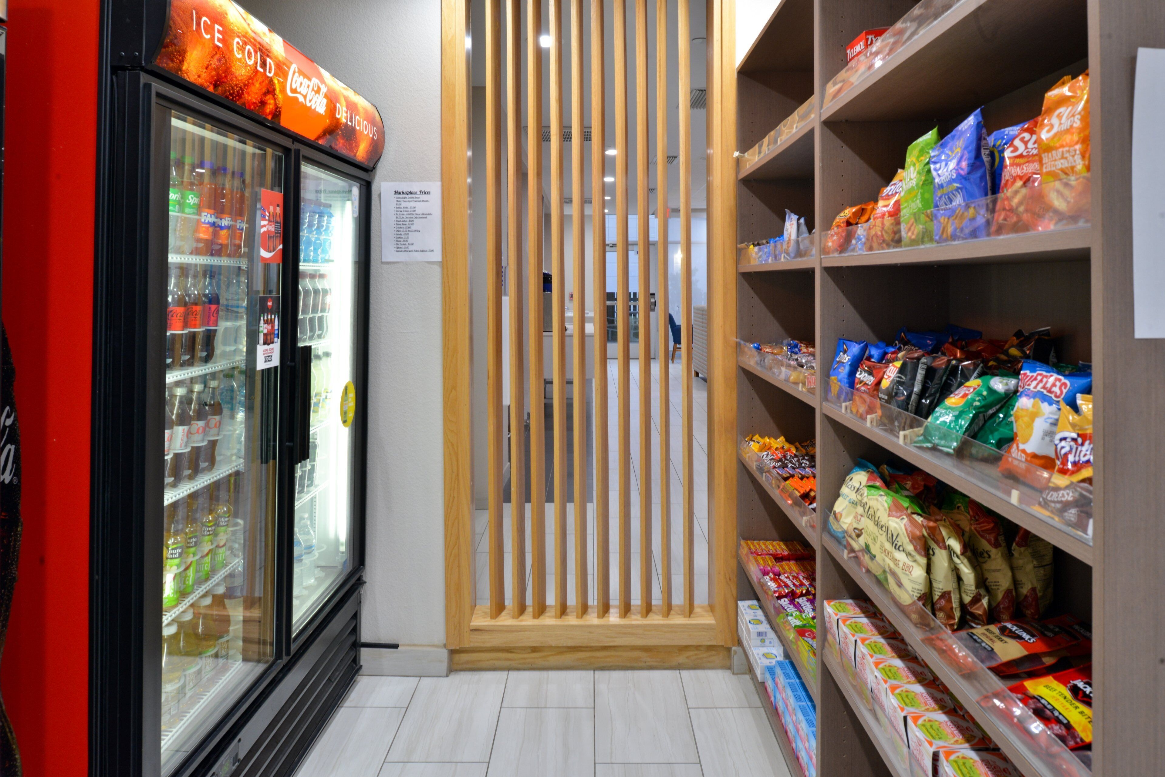 Mostrador refrigerado con diversas bebidas, una partición de madera y estantes llenos de aperitivos.