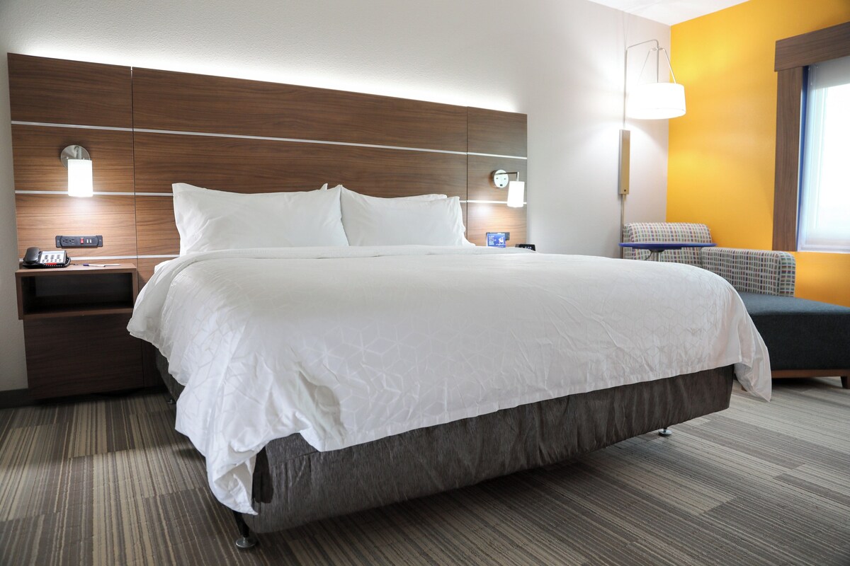 A hotel room with a large bed, bedside tables, a nightstand, a lamp, and a window.