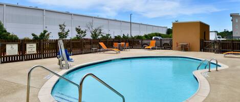 A swimming pool with a wooden fence, lounge chairs, and a lifeguard stand.
