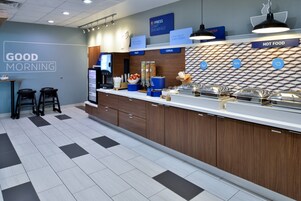Una cocina moderna con barra americana, señalización identificando desayuno y comida caliente, y un revestimiento de pared con diseño.