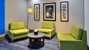 Een kamer met drie groene fauteuils, een klein rond tafeltje met zakdoosjes, en drie kunstwerken in lijsten aan de muur.