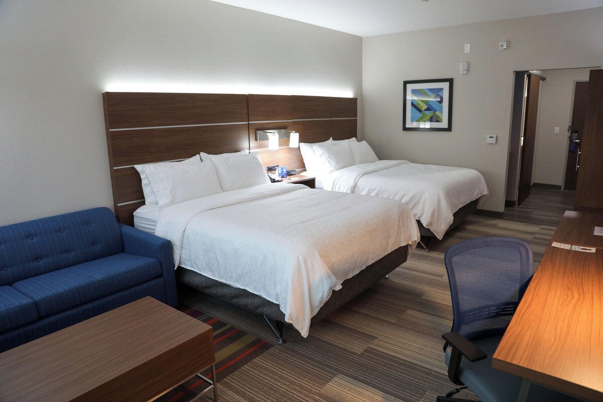 A hotel room with two beds, a blue sofa, a wooden desk, and a chair.