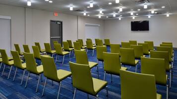 A conference room with rows of green chairs, a whiteboard, a projector screen, and a flat-screen TV on the wall.