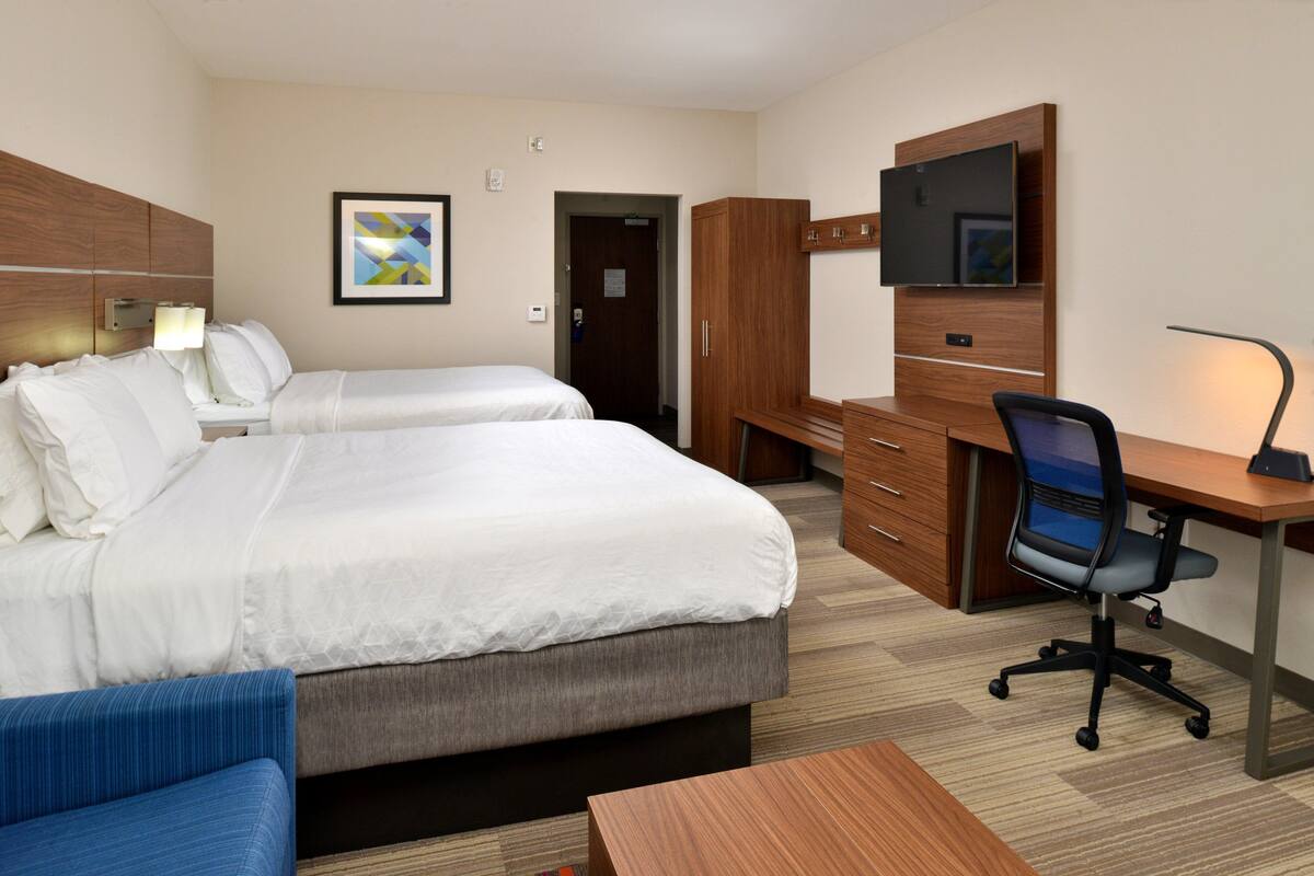 A hotel room with two beds, a desk, a chair, a TV, and a wardrobe.