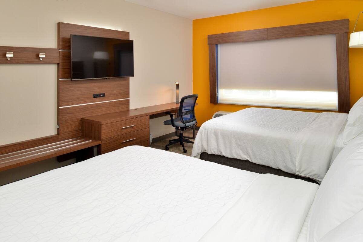 A hotel room with a bed, a desk with a chair, a TV, and a window with blinds.