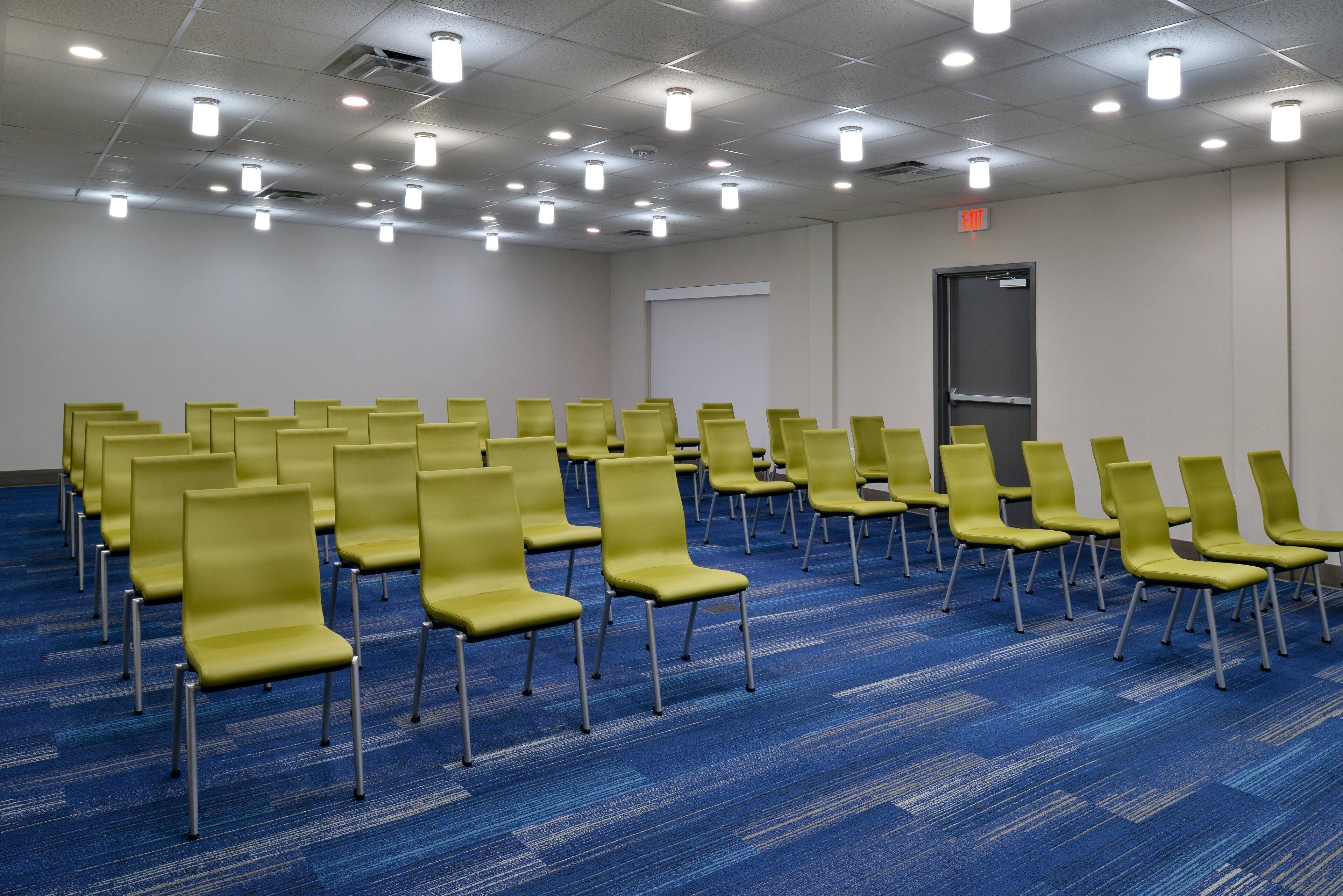A conference room with rows of yellow chairs, a blue carpet, and a white ceiling with multiple lights.