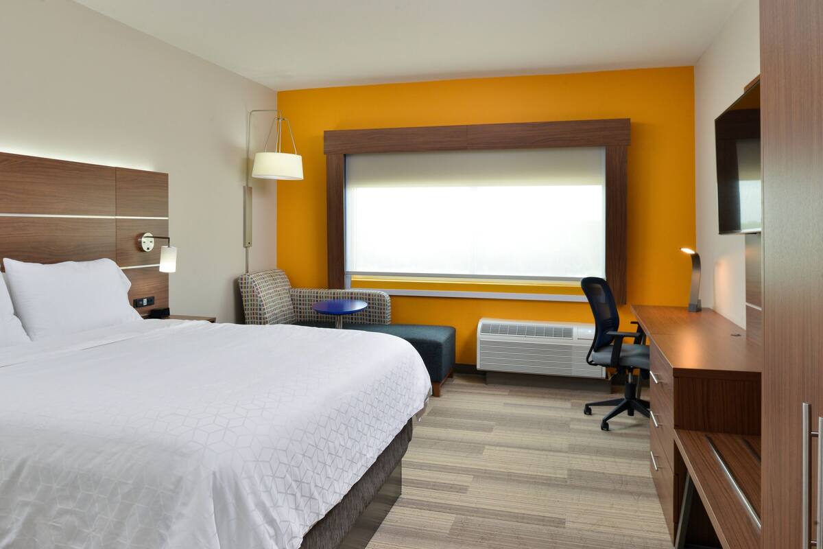 A hotel room with a large bed, a desk, a chair, a small table, and a TV.