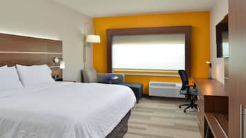 A hotel room with a large bed, a desk, a chair, a small table, and a TV.