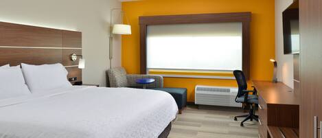 A hotel room with a large bed, a desk, a chair, a small table, and a TV.