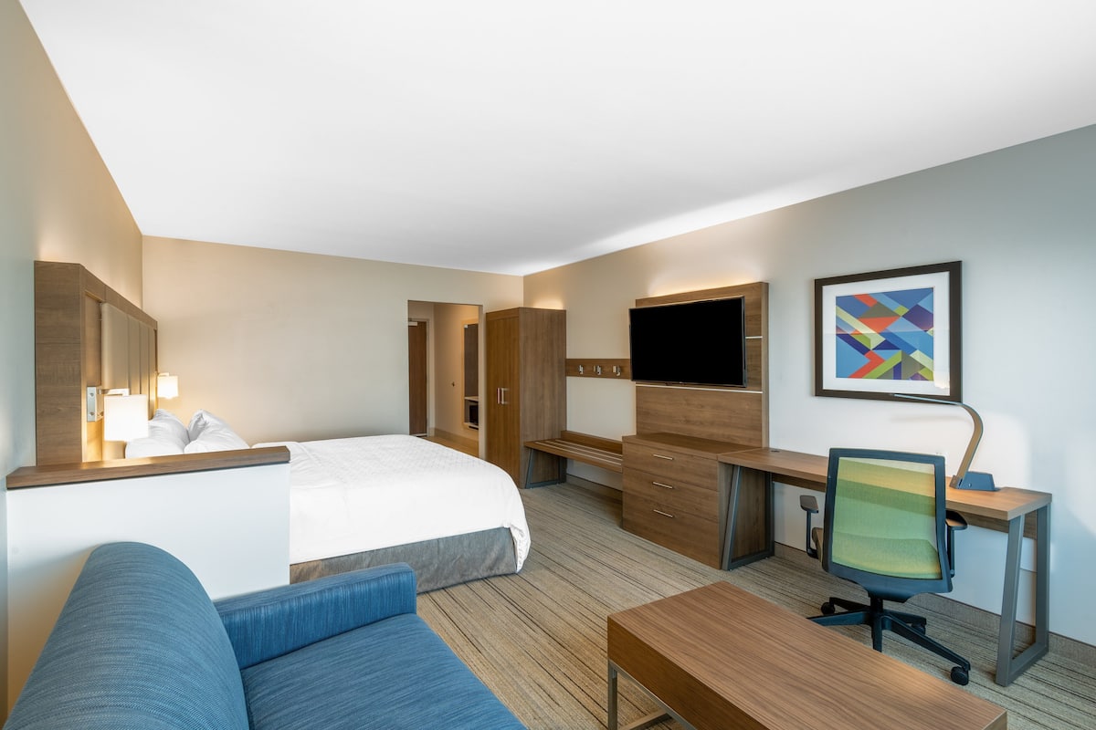 A hotel room with a bed, a desk, a chair, a TV, and a painting on the wall.
