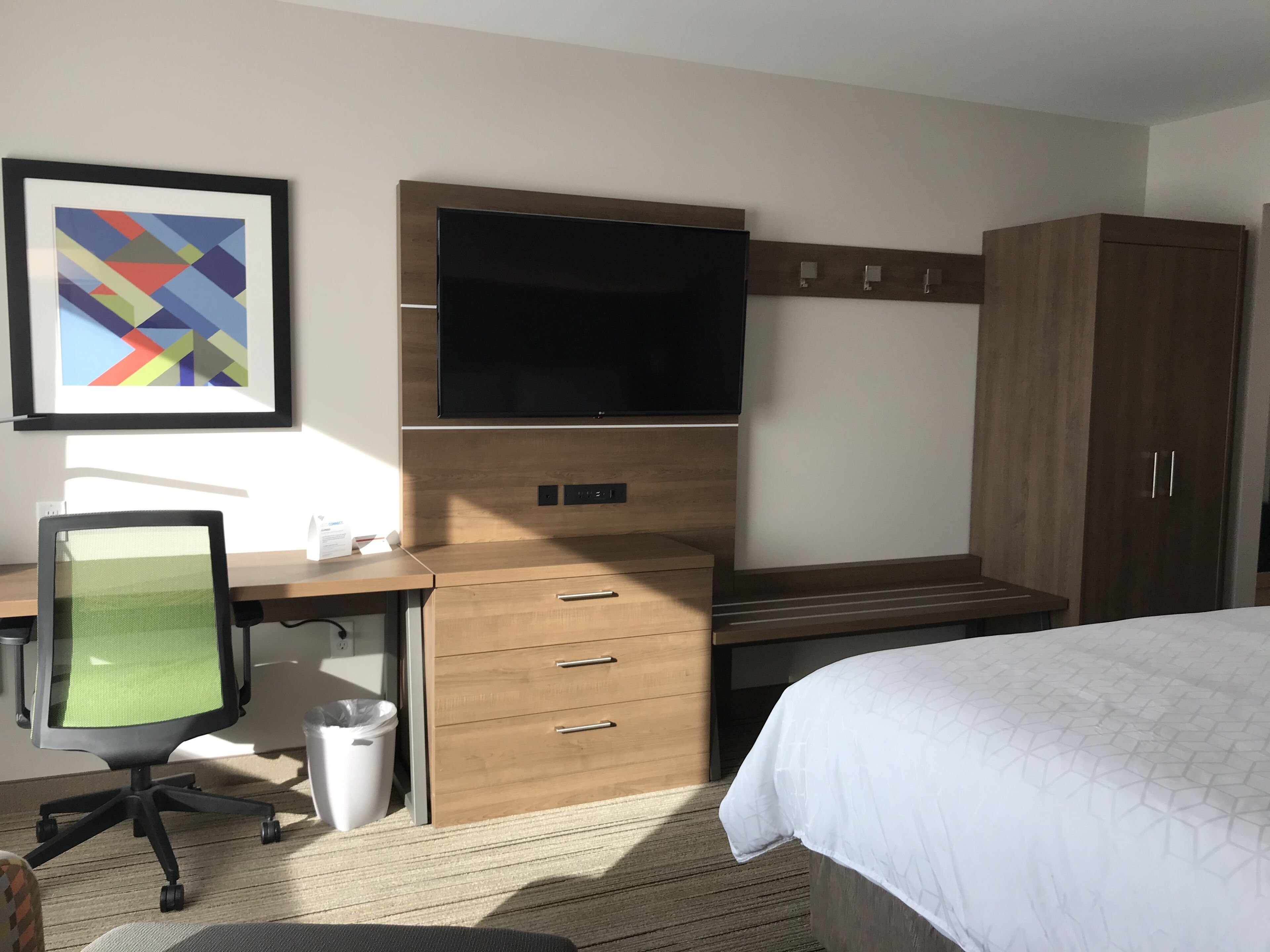 A hotel room with a bed, a desk with a computer, a TV, and a wardrobe.