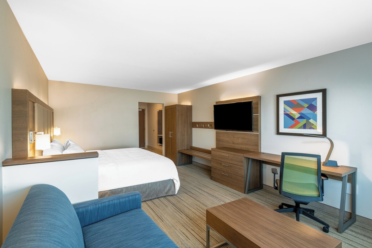 A hotel room with a bed, a desk, a chair, a TV, and a painting on the wall.