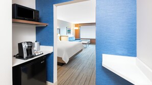 A hotel room with a bed, a coffee machine, a microwave, and a TV on a shelf.