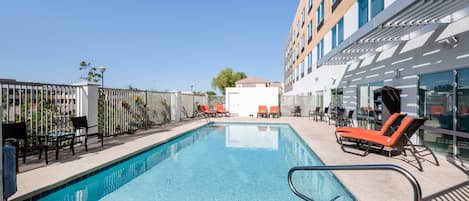 A rooftop swimming pool with lounge chairs and a building in the background.