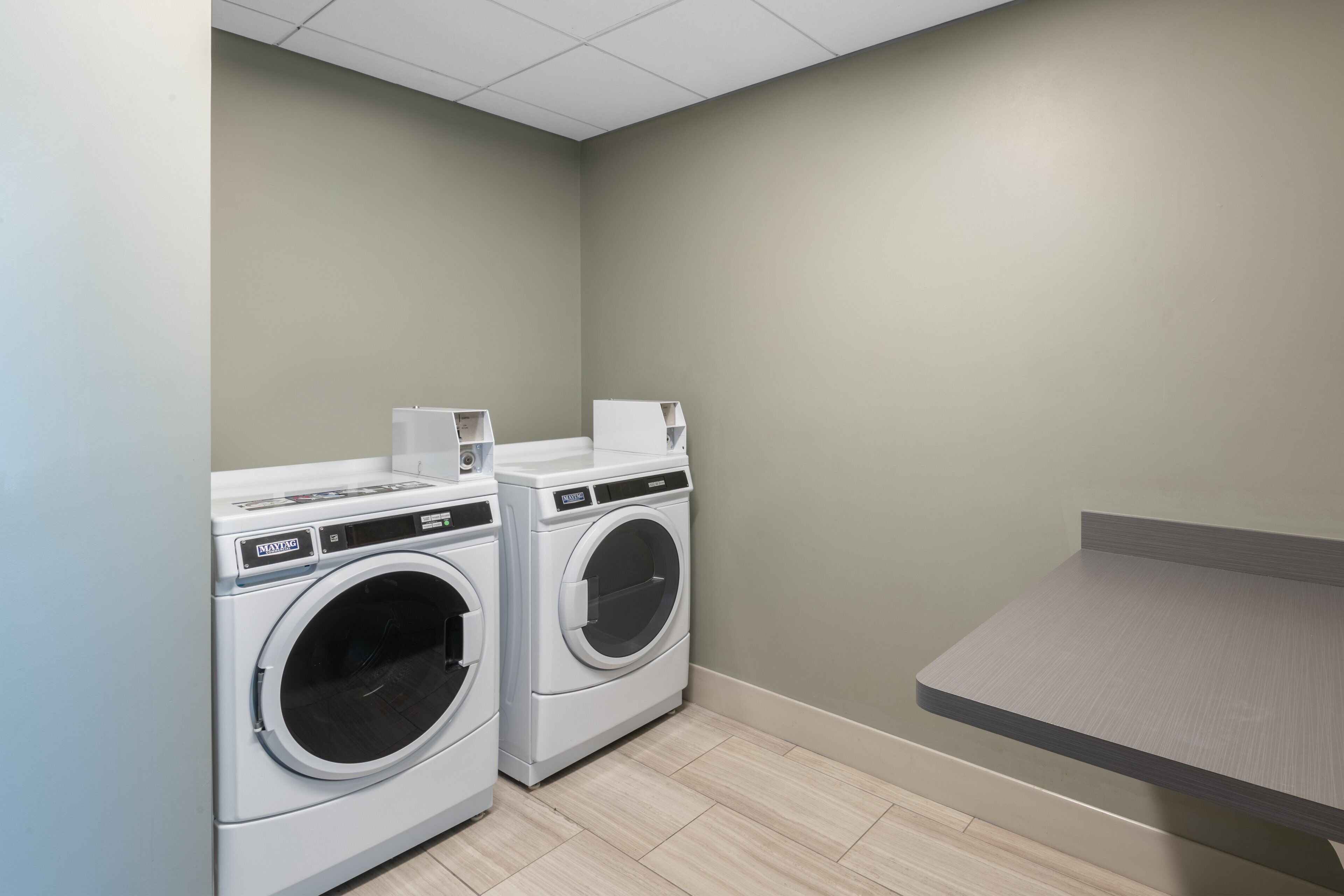 A laundry room with two front-loading washing machines, a small shelf with a cup, and a grey countertop.