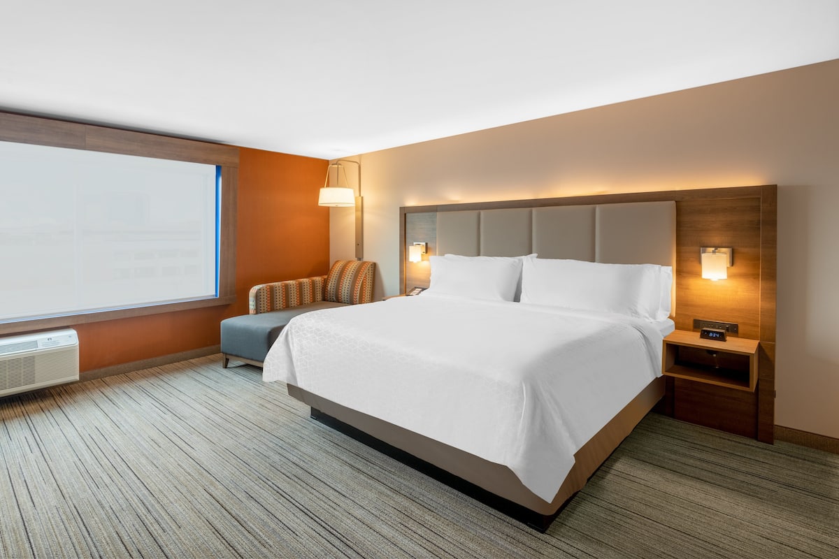 A hotel room with a large bed, a nightstand, a lamp, and a window.