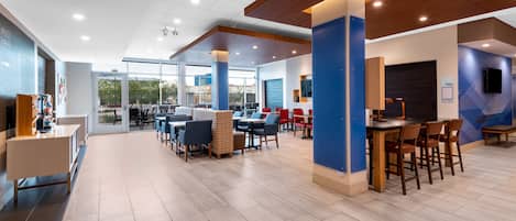 A spacious, modern lounge area with multiple seating arrangements, including tables and chairs, and a large window providing a view of the outdoors.