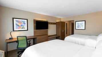 A hotel room with two beds, a desk with a computer, a TV, and artwork on the walls.