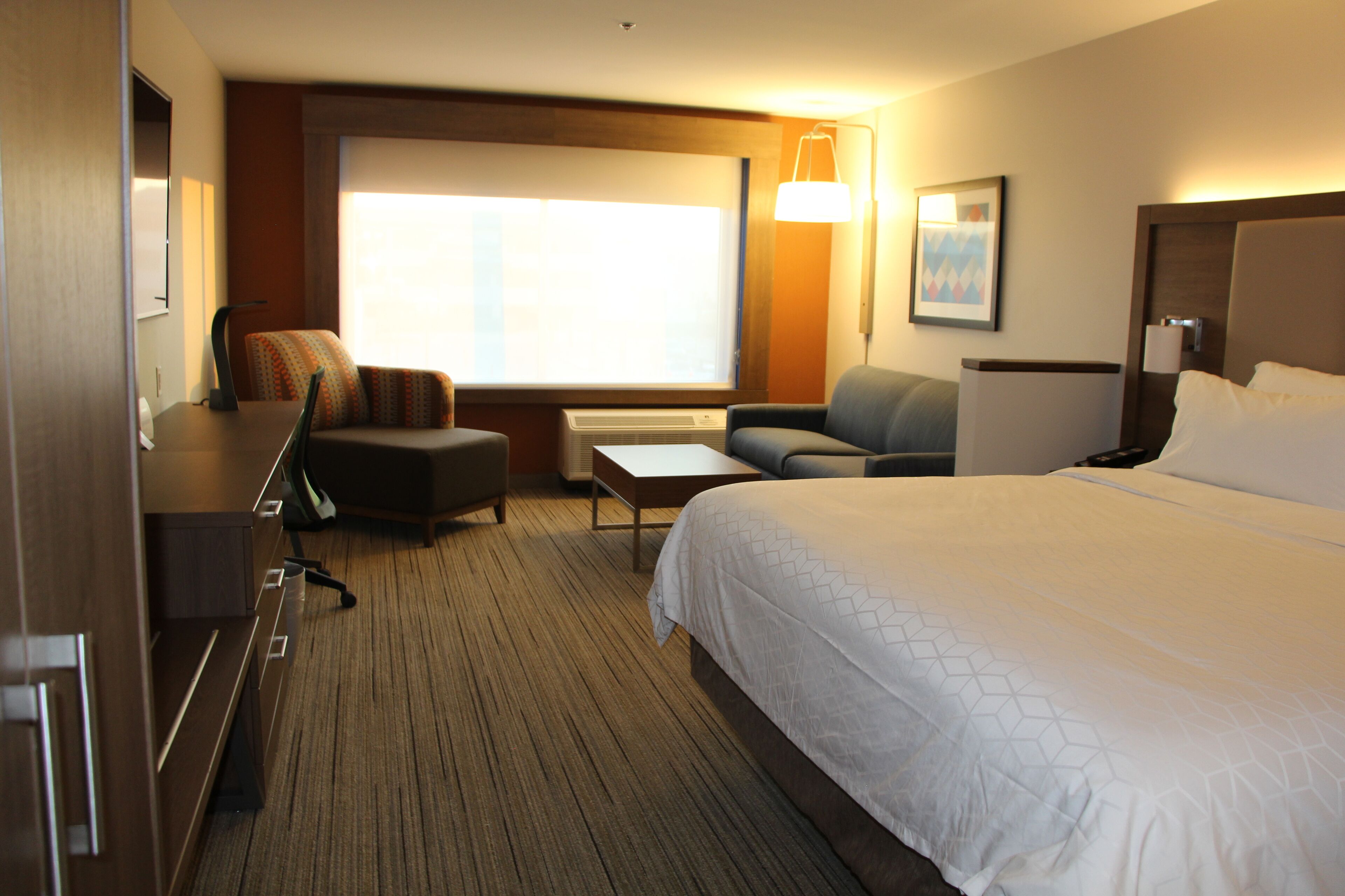 A hotel room with a large bed, a desk, a chair, a sofa, and a TV.