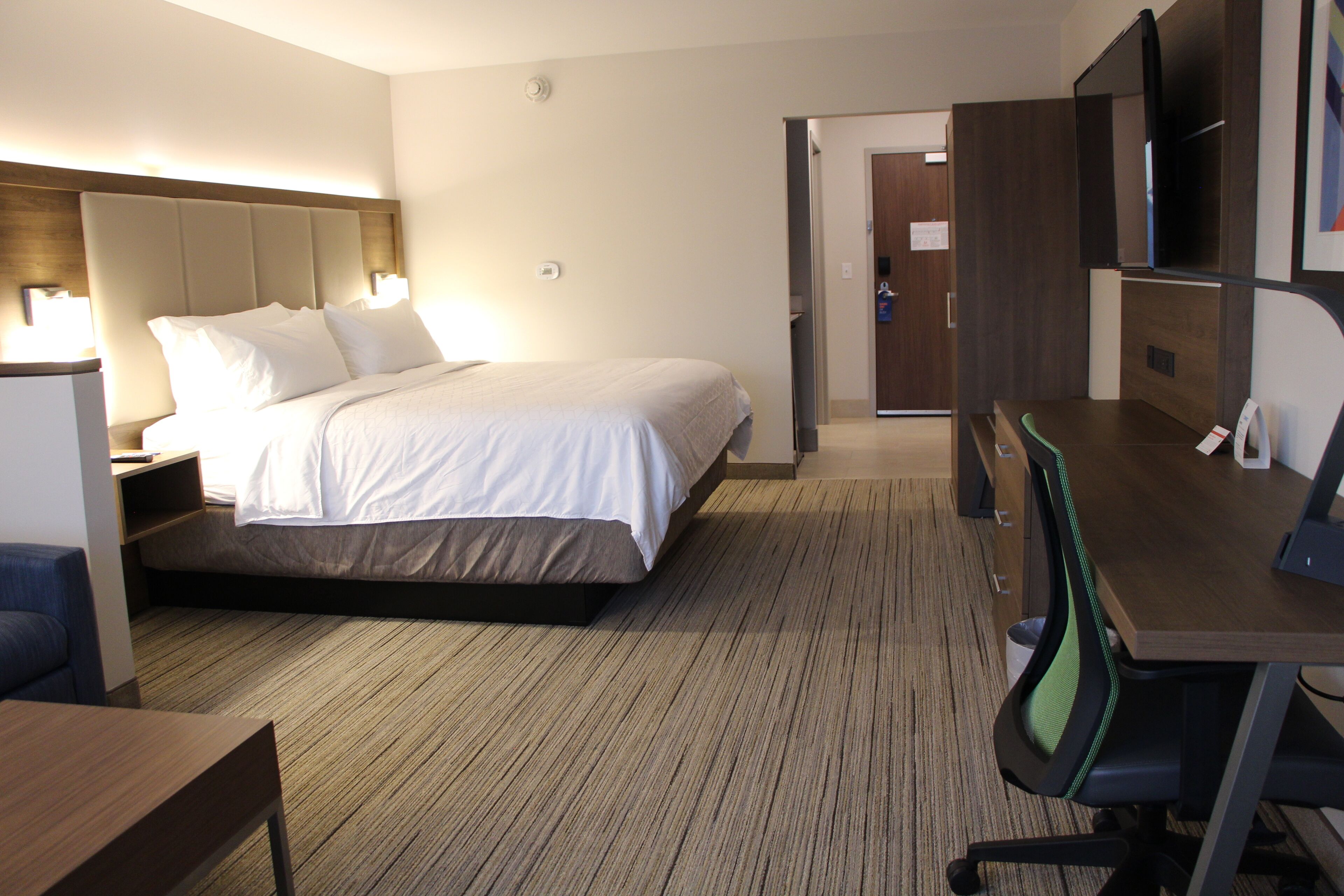 A hotel room with a bed, bedside table, lamp, desk, chair, and a television.