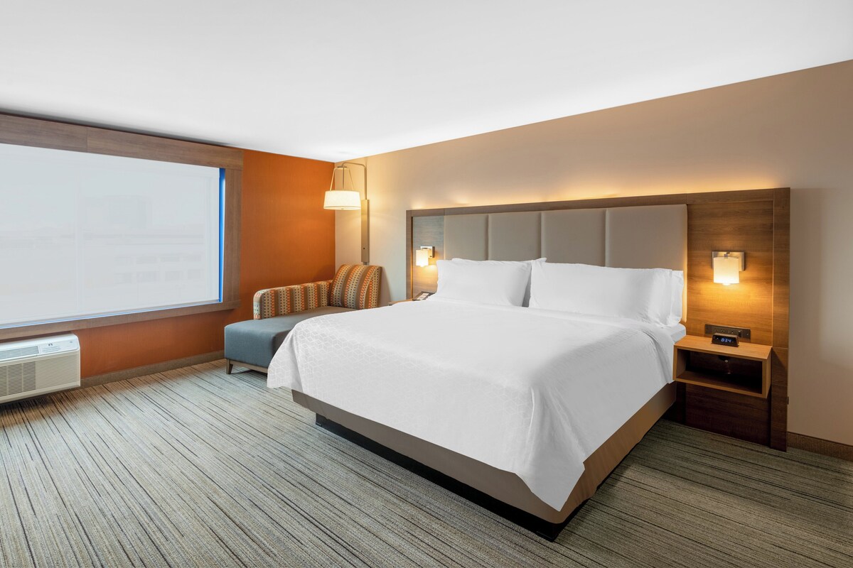 A hotel room with a large bed, a nightstand, a lamp, and a window.