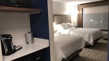 Quarto de hotel com cozinha compacta, duas camas, uma janela grande e televisão na parede.