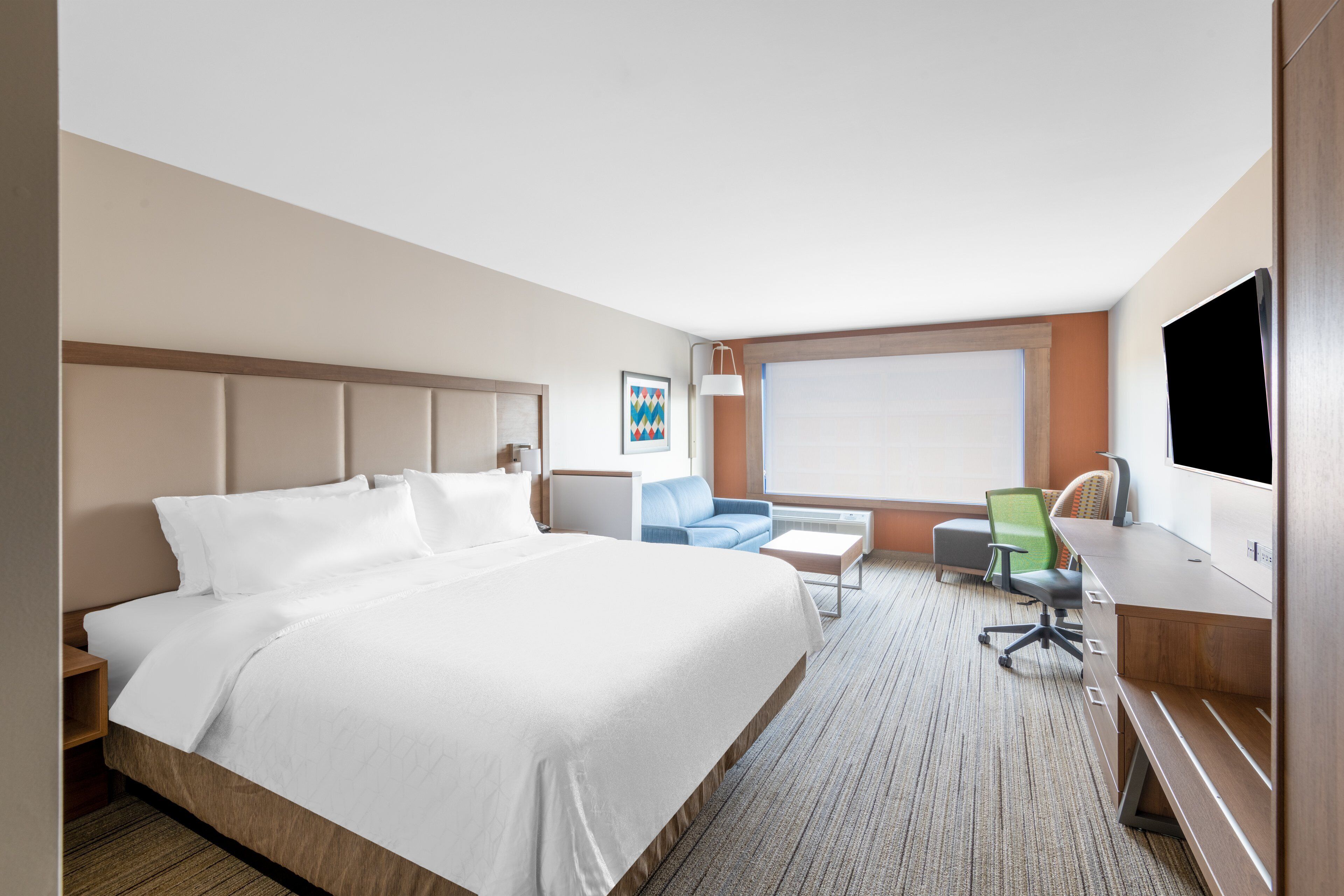 A hotel room with a large bed, a desk, a chair, a small table, and a TV.