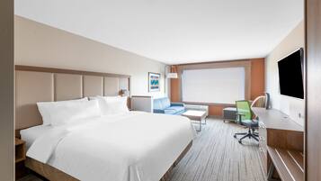 A hotel room with a large bed, a desk, a chair, a small table, and a TV.