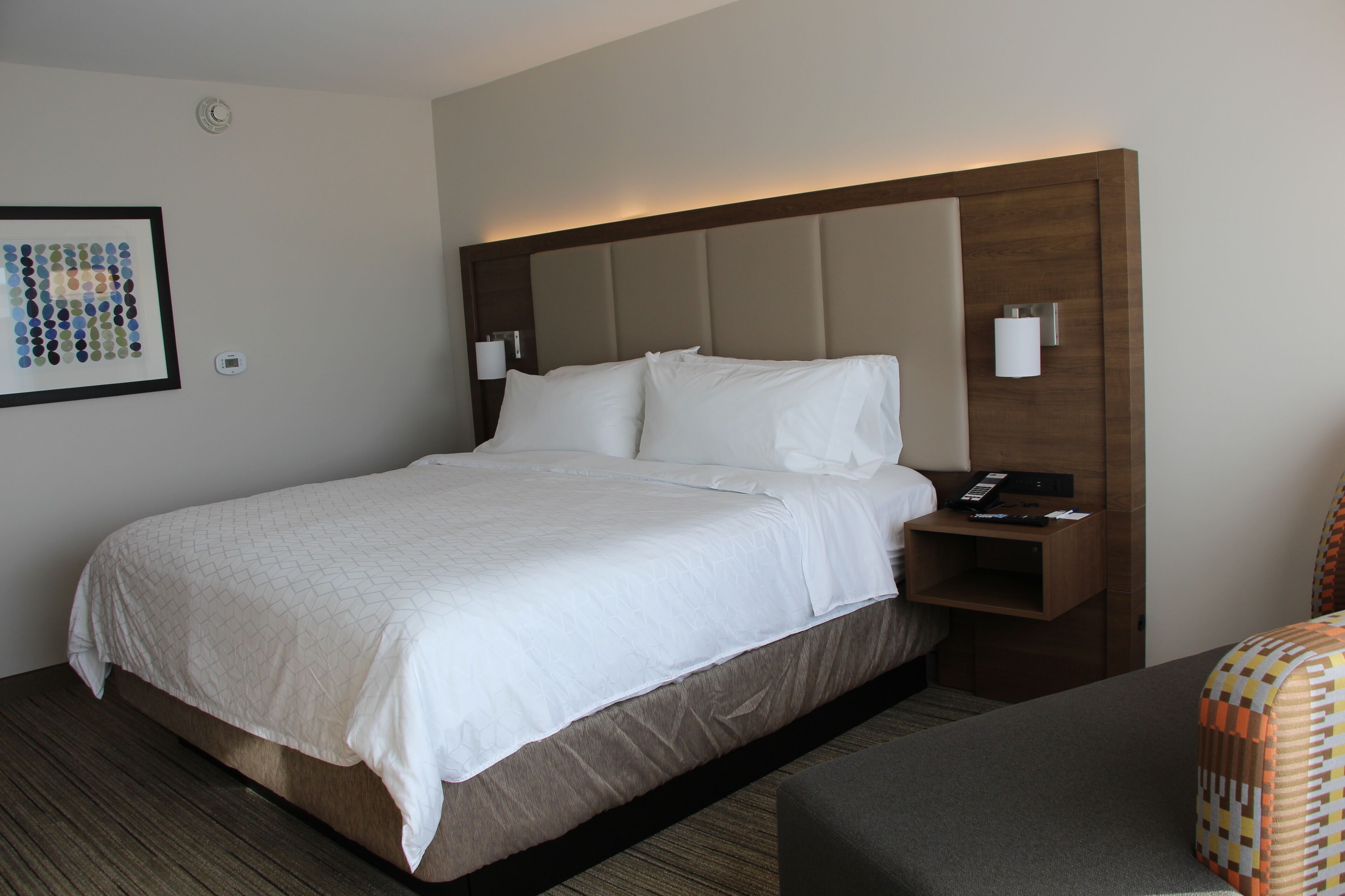 A neatly made bed with a wooden headboard, a bedside table with a lamp, and a framed picture on the wall.