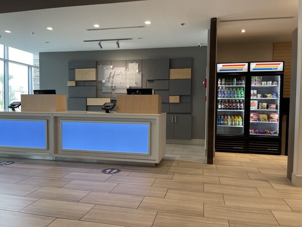 A hotel reception area with a modern design, including a reception desk, a digital display, and a beverage refrigerator.