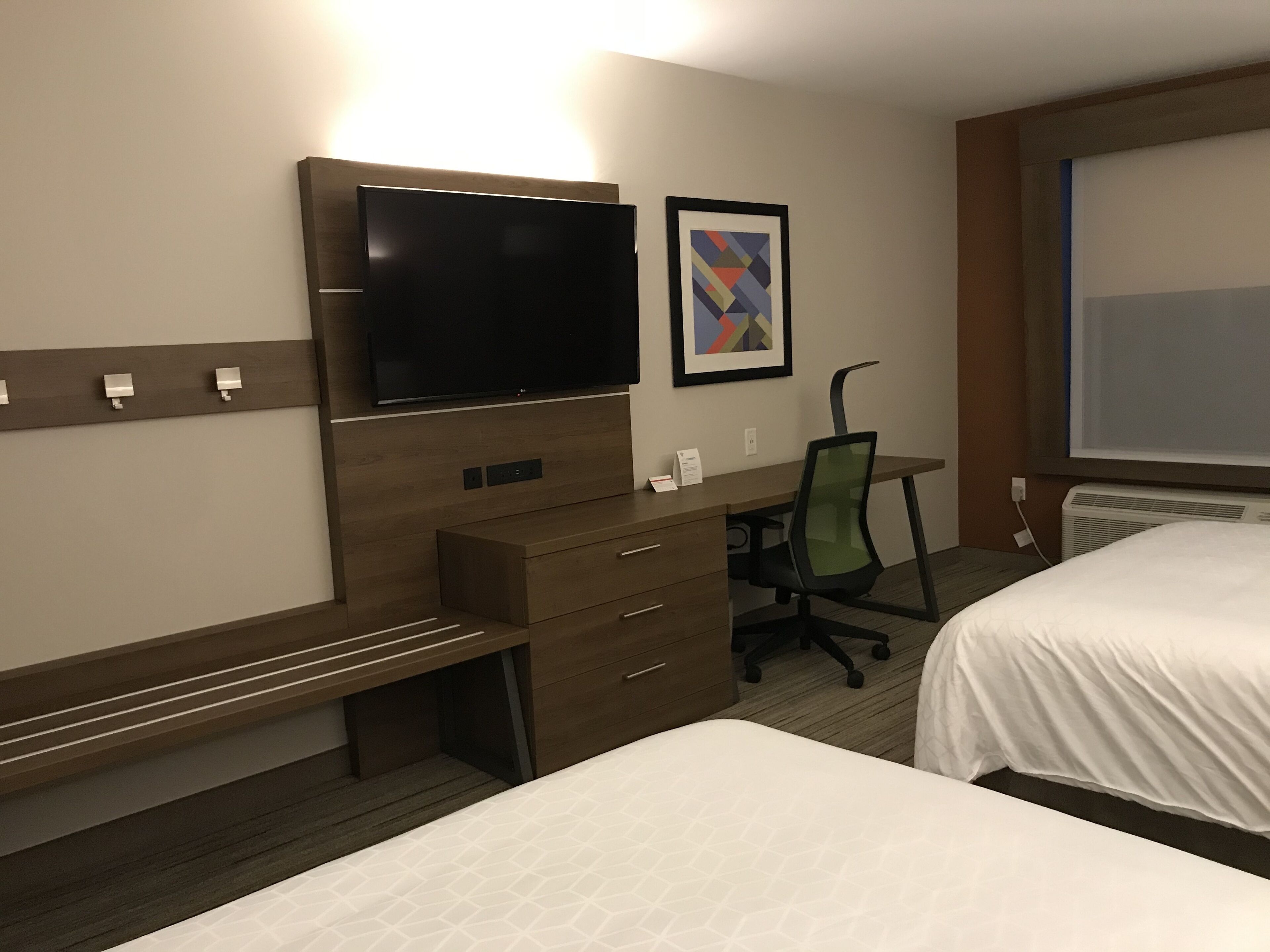A hotel room with a bed, a desk with a chair, a television, and a framed picture on the wall.