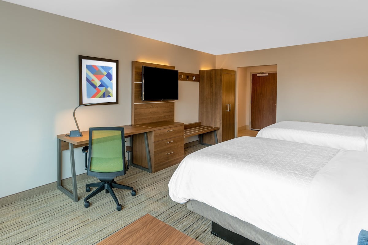 A hotel room with a bed, a desk with a chair, a TV mounted on the wall, and a wardrobe.