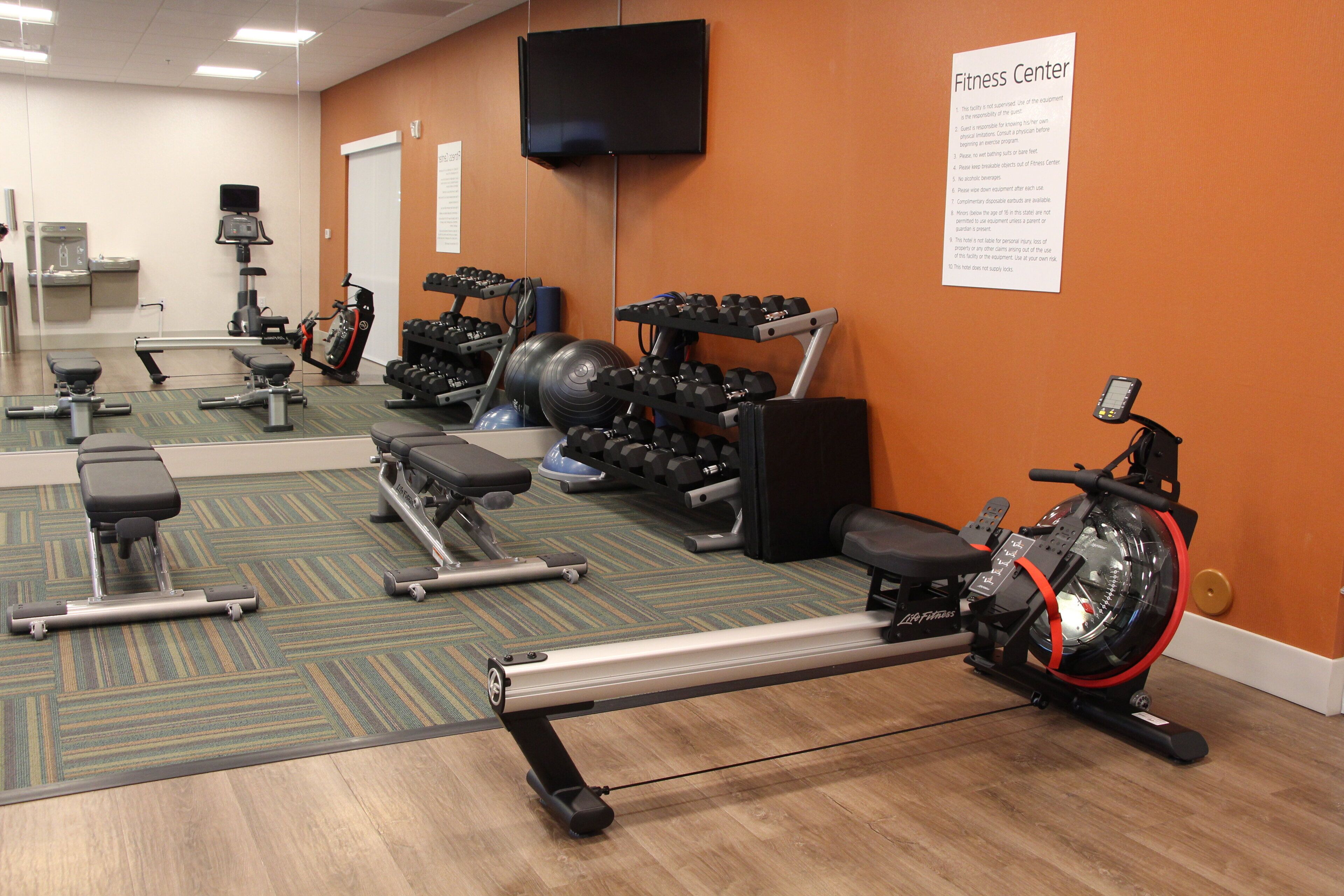 A fitness center with exercise equipment, a mirror, and a sign listing rules.