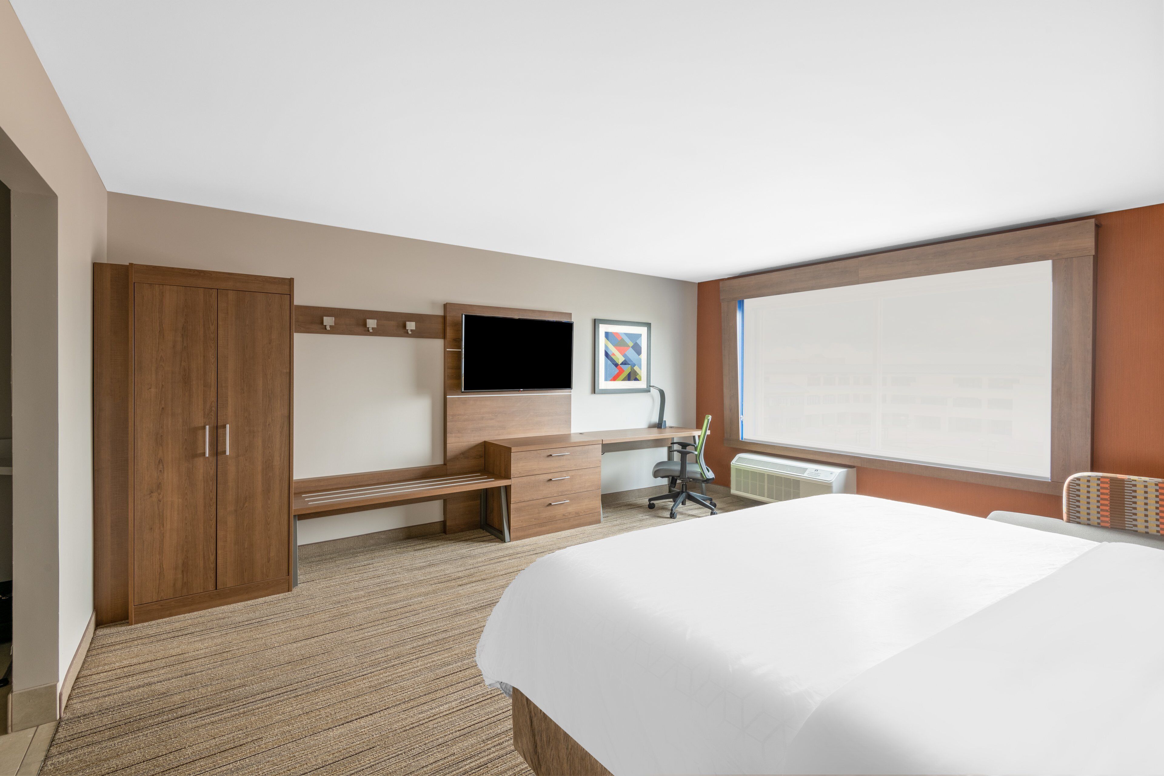 Habitación de hotel con cama, escritorio, silla, armario, televisor y ventana.