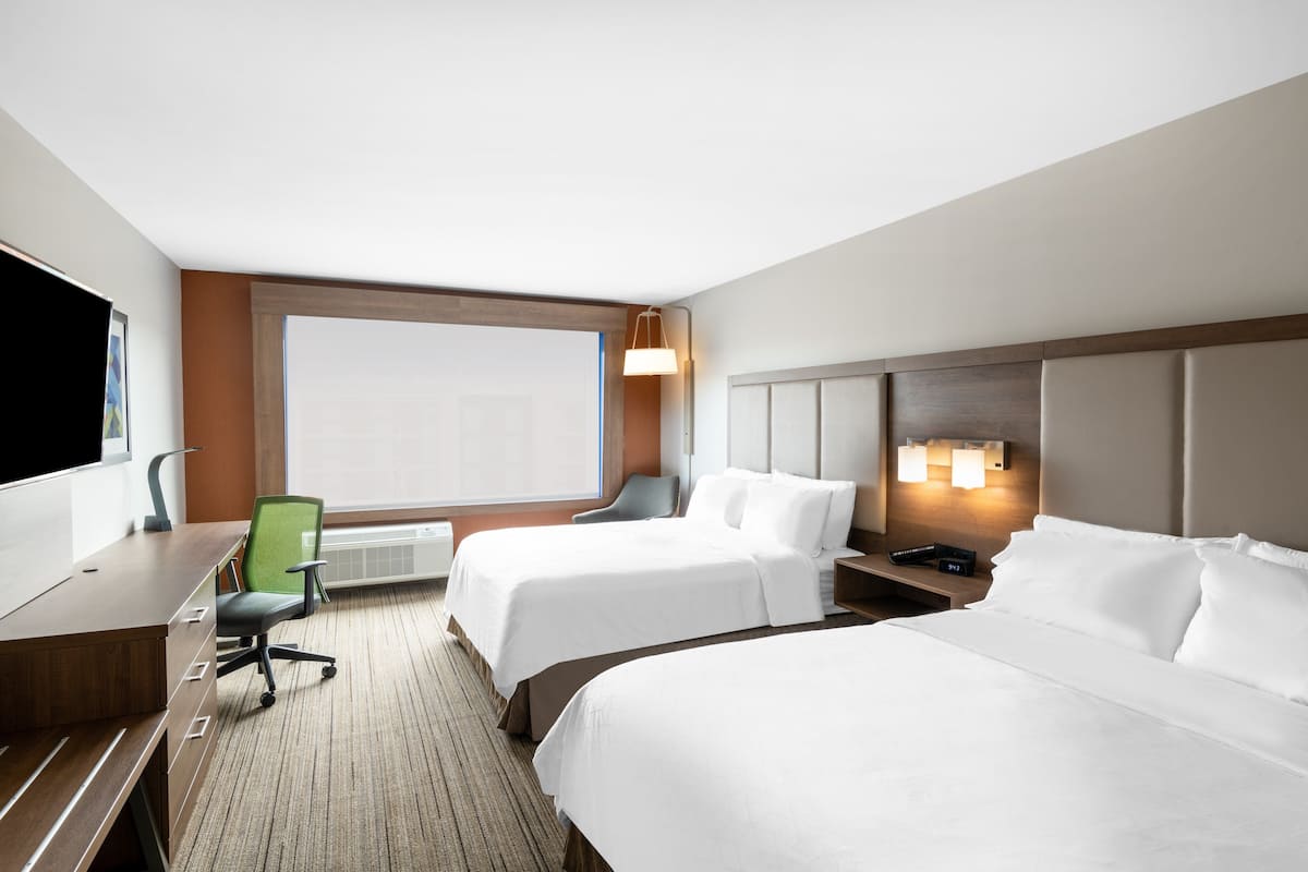 A hotel room with two beds, a desk, a chair, a TV, and a large window.