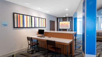Bancada de recepção com um computador, duas cadeiras e uma placa indicando um centro de negócios.