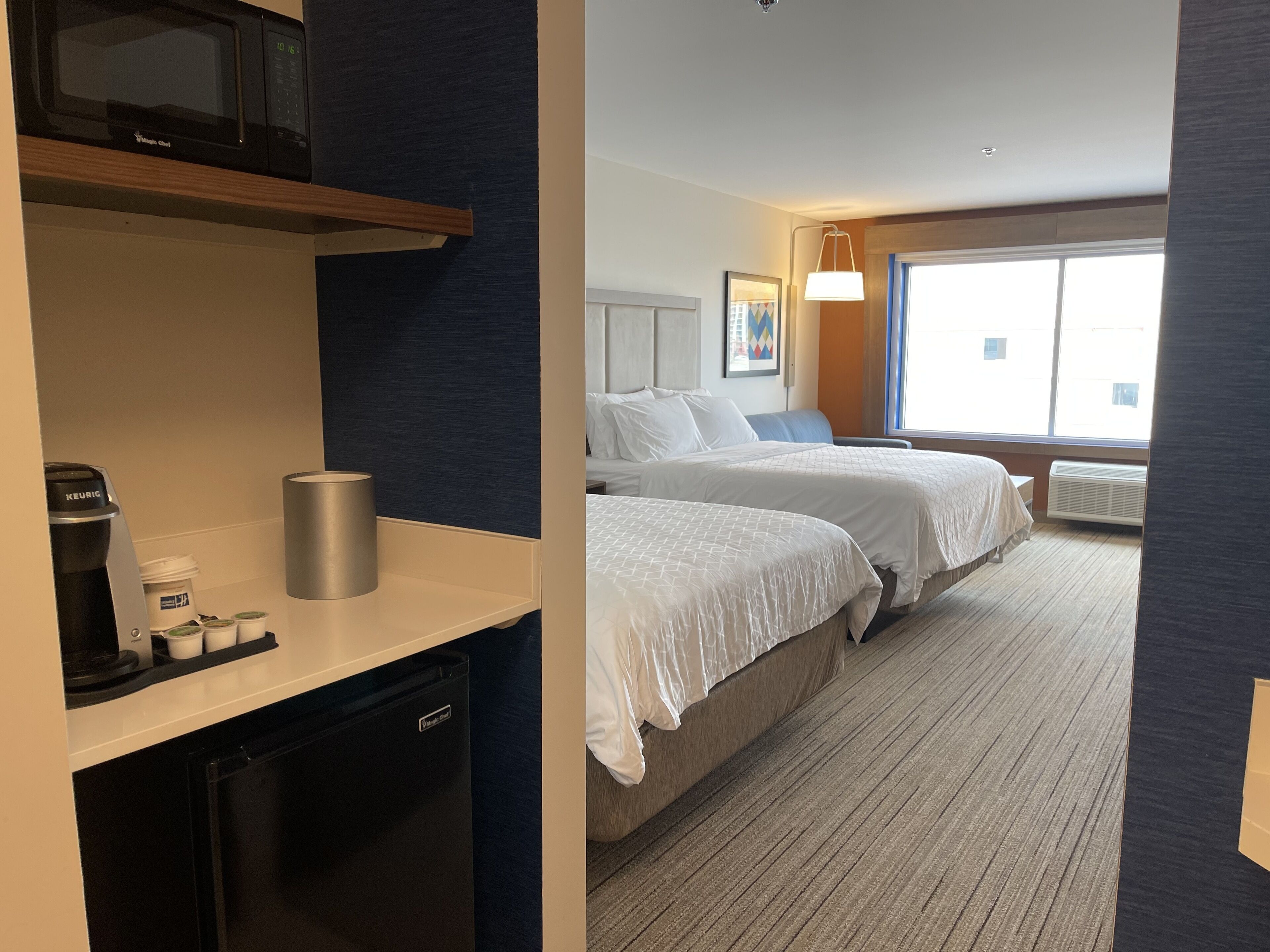 Une chambre d’hôtel avec une kitchenette, deux lits, une grande fenêtre et une vue sur la ville.
