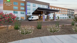 A Holiday Inn Express & Suites building with a covered entrance, a parking lot, and landscaped areas with flowers. - Holiday Inn Express & Suites Phoenix - Airport North by IHG (Phoenix)