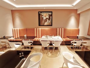 A modern dining area with a long table, white chairs, and a bench. - Mallige Residency (Hassan)