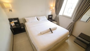 Habitació d'hotel amb un llit, taules de nit, una làmpada i una finestra amb cortines.