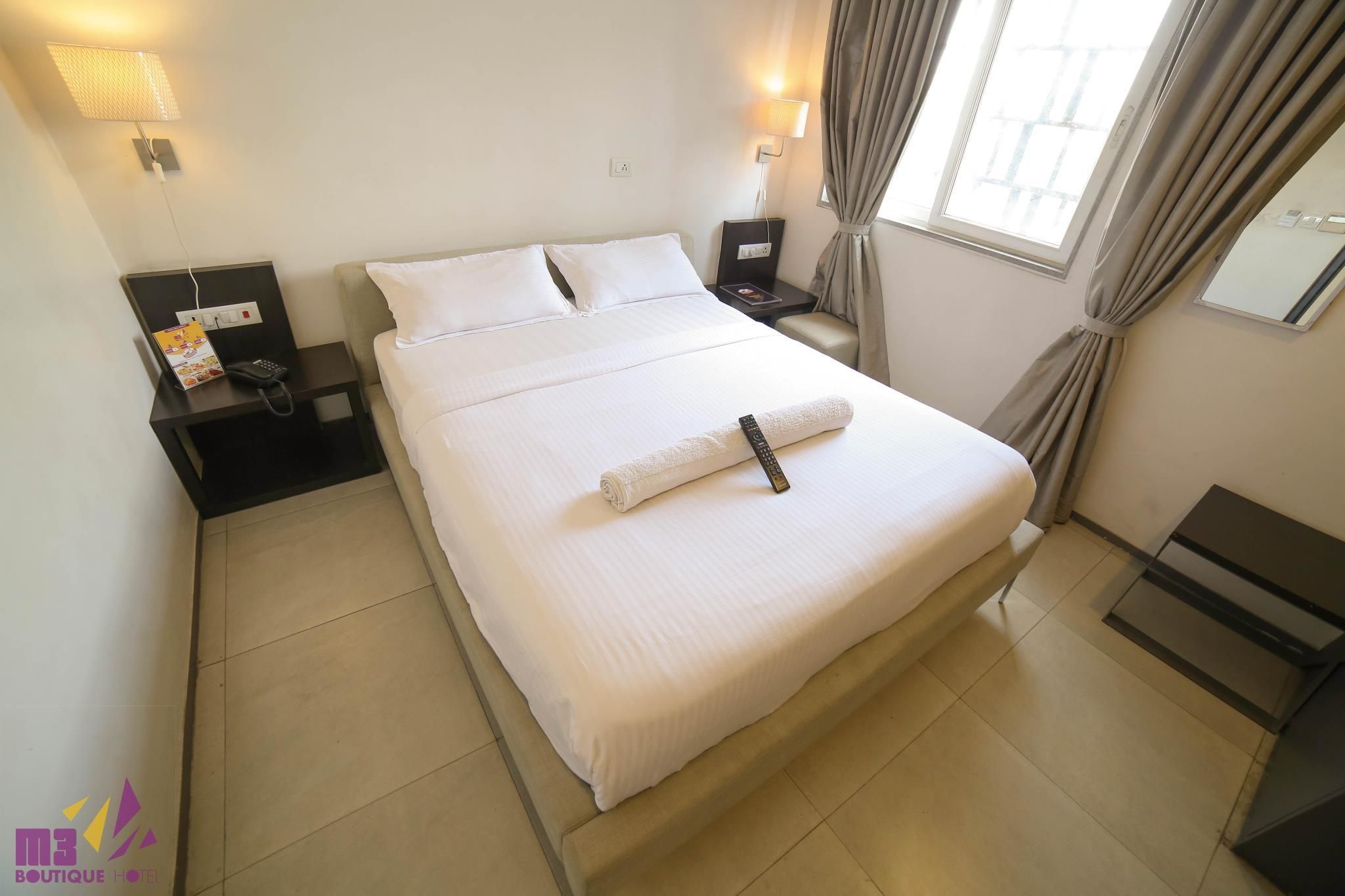 A hotel room with a bed, bedside tables, a lamp, and a window with curtains.